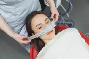 Dental assistant fitting a sedation mask over the nose of her calm female patient at Virginia Surgical Arts in Virginia Beach, VA.