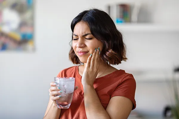 Young woman holding her jaw and wincing in pain from TMJ